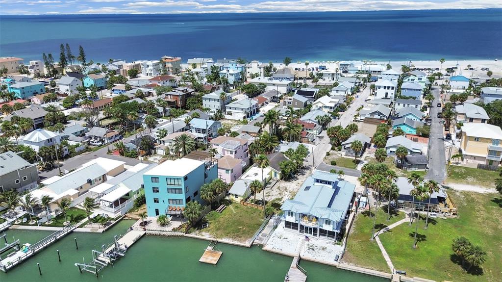 An aerial view shows waterfront homes with docks along a canal near a sandy beach — 130 90TH AVENUE, TREASURE ISLAND, FL