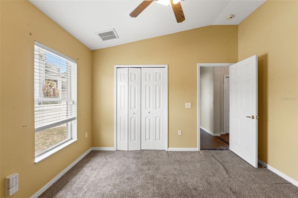 A bedroom with yellow walls, carpeted flooring, a window, a closet, and an open door — 4490 AYRSHIRE DRIVE, SPRING HILL, FL