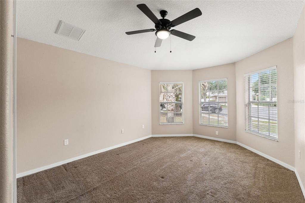 An empty bedroom features beige walls, brown carpet, a ceiling fan, and three large windows — 4490 AYRSHIRE DRIVE, SPRING HILL, FL
