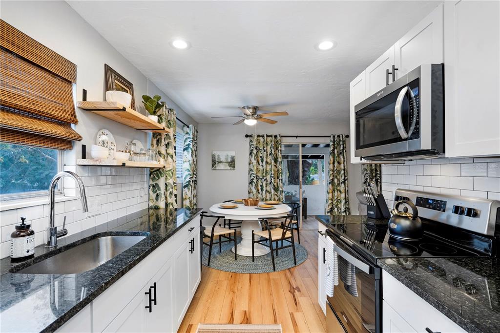 A kitchen with white cabinets, dark granite countertops, and a dining area with a round table — 4705 HOLLINGSWORTH AVENUE, SARASOTA, FL