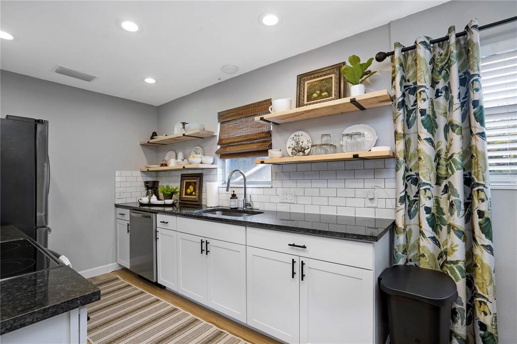 A kitchen features white cabinets, black countertops, open wood shelving, and a subway tile backsplash — 4705 HOLLINGSWORTH AVENUE, SARASOTA, FL