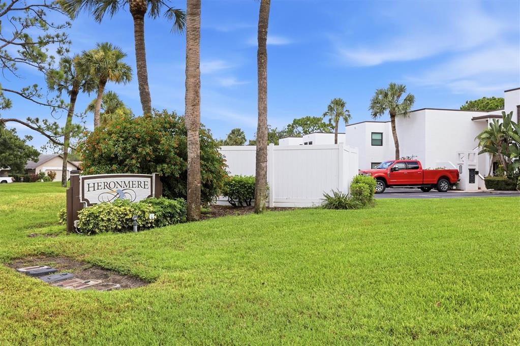 A sign for Heronmere stands in a grassy yard before a white building and truck — 3508 RICHWOOD LINK UNIT 55, SARASOTA, FL