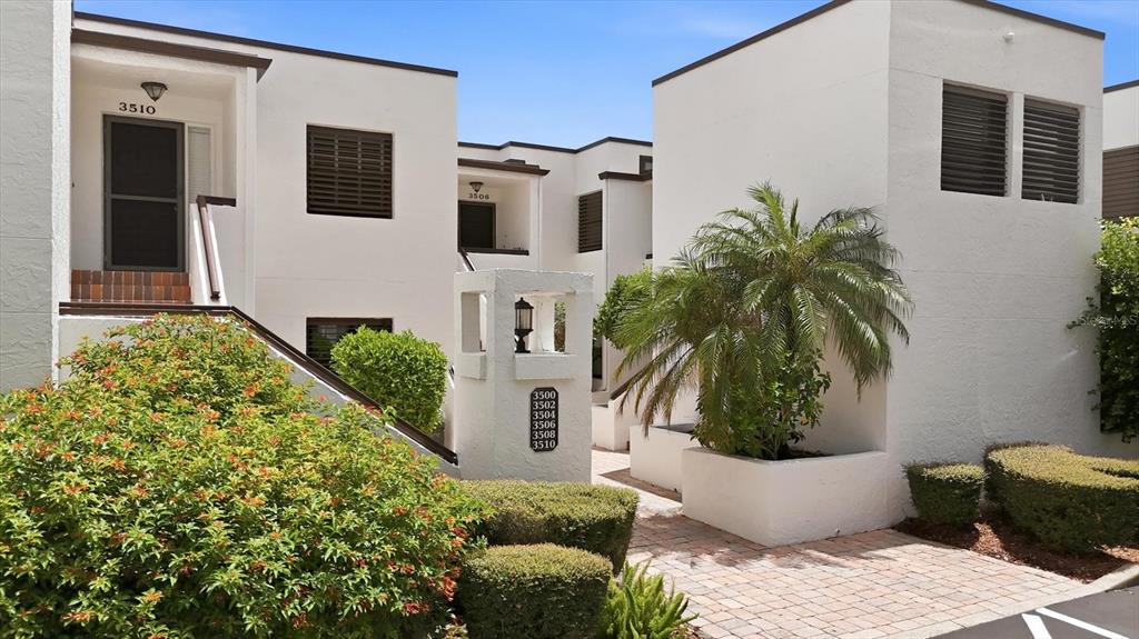 A multi-unit residential building with white stucco walls, dark shutters, and a brick walkway — 3508 RICHWOOD LINK UNIT 55, SARASOTA, FL