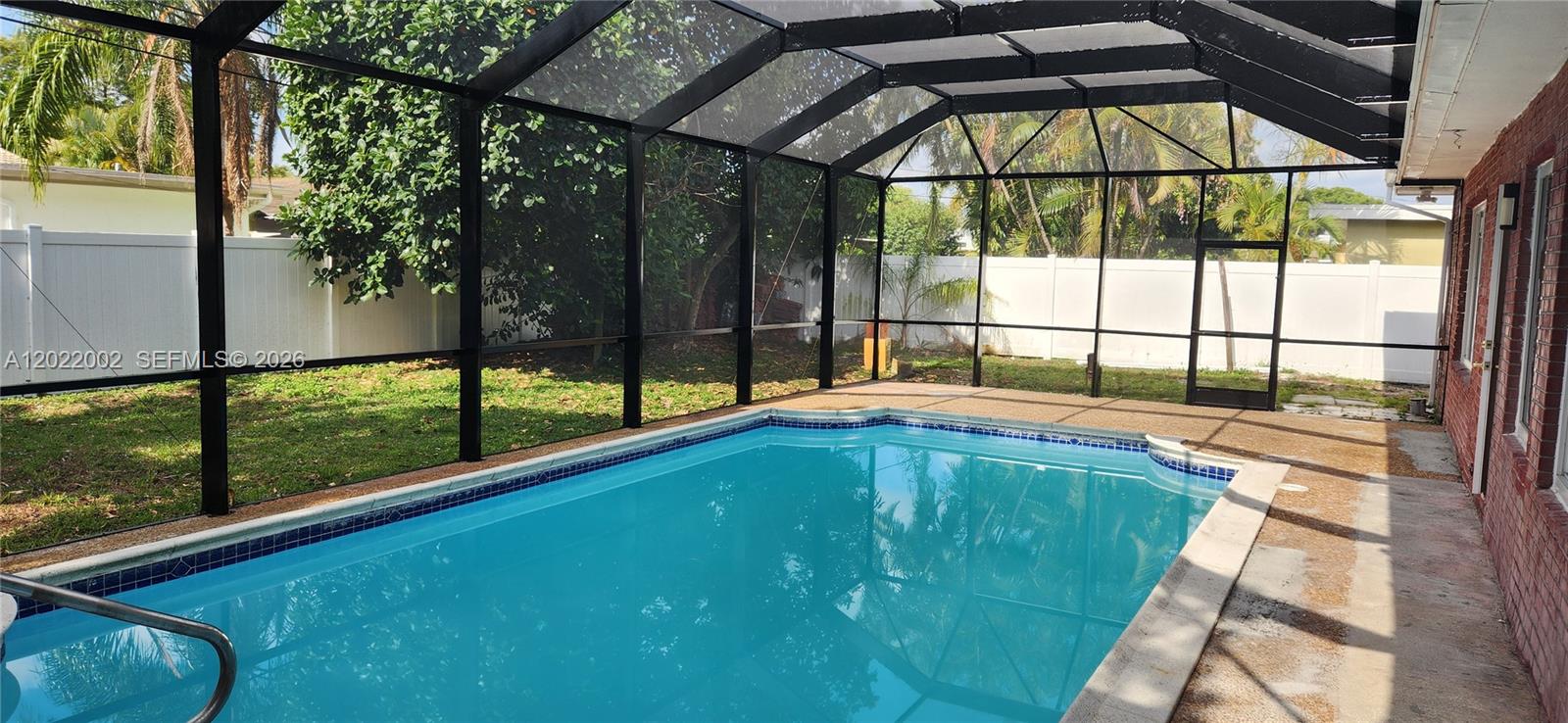 A rectangular swimming pool is enclosed by a screened lanai with a white vinyl fence — 5260 SW 9th St, Plantation FL 33317, PLANTATION, FL