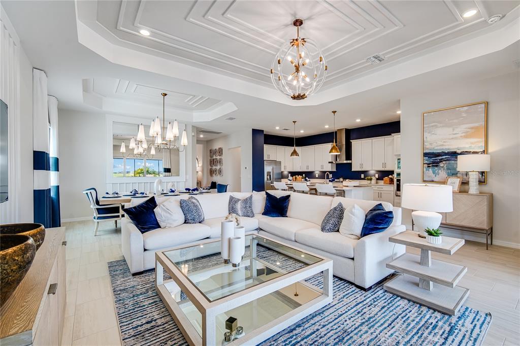 A bright, open-concept living room features a white sectional sofa, blue accents, and tray ceilings — 7165 INLET ISLES COURT, LAKEWOOD RANCH, FL