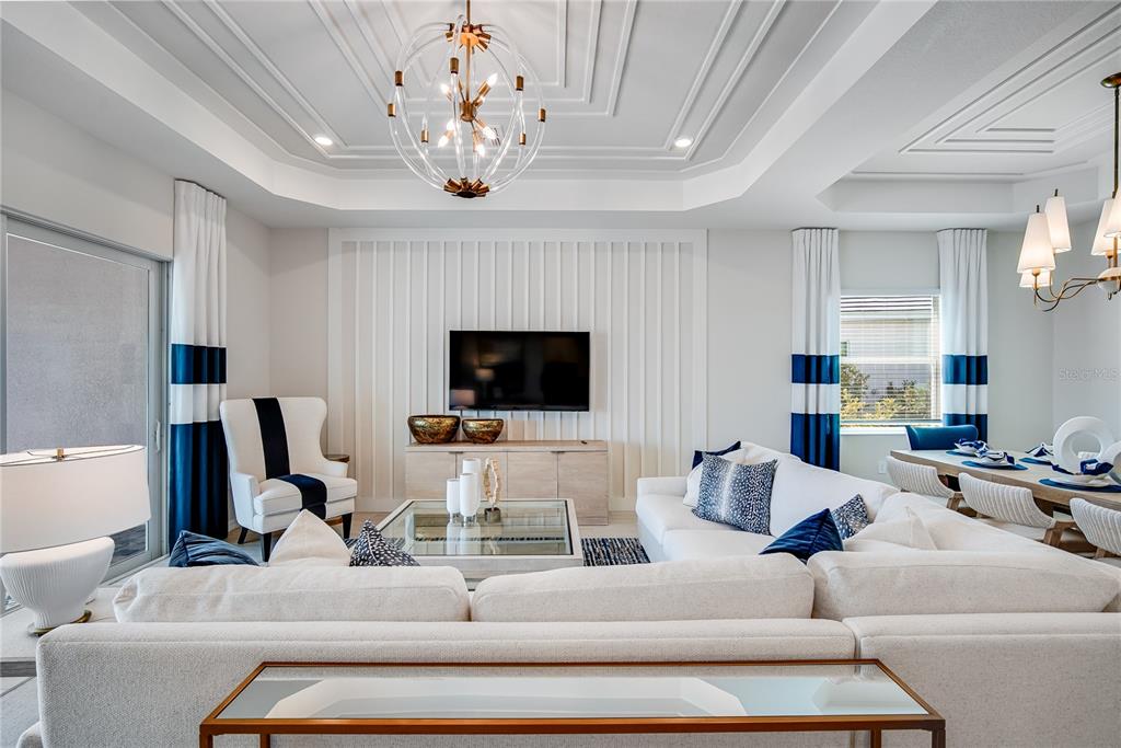 A living room features a coffered ceiling, a wall-mounted television, and a white sectional sofa — 7165 INLET ISLES COURT, LAKEWOOD RANCH, FL