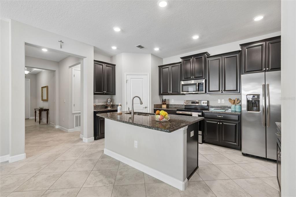 A kitchen with dark wood cabinets, granite countertops, stainless steel appliances, and tile flooring — 9908 SAGE CREEK DRIVE, RUSKIN, FL