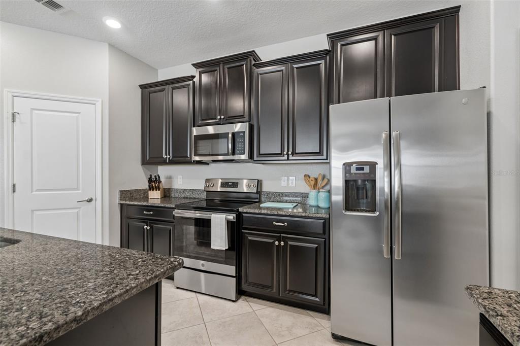 A kitchen features dark wood cabinets, granite countertops, and stainless steel appliances — 9908 SAGE CREEK DRIVE, RUSKIN, FL