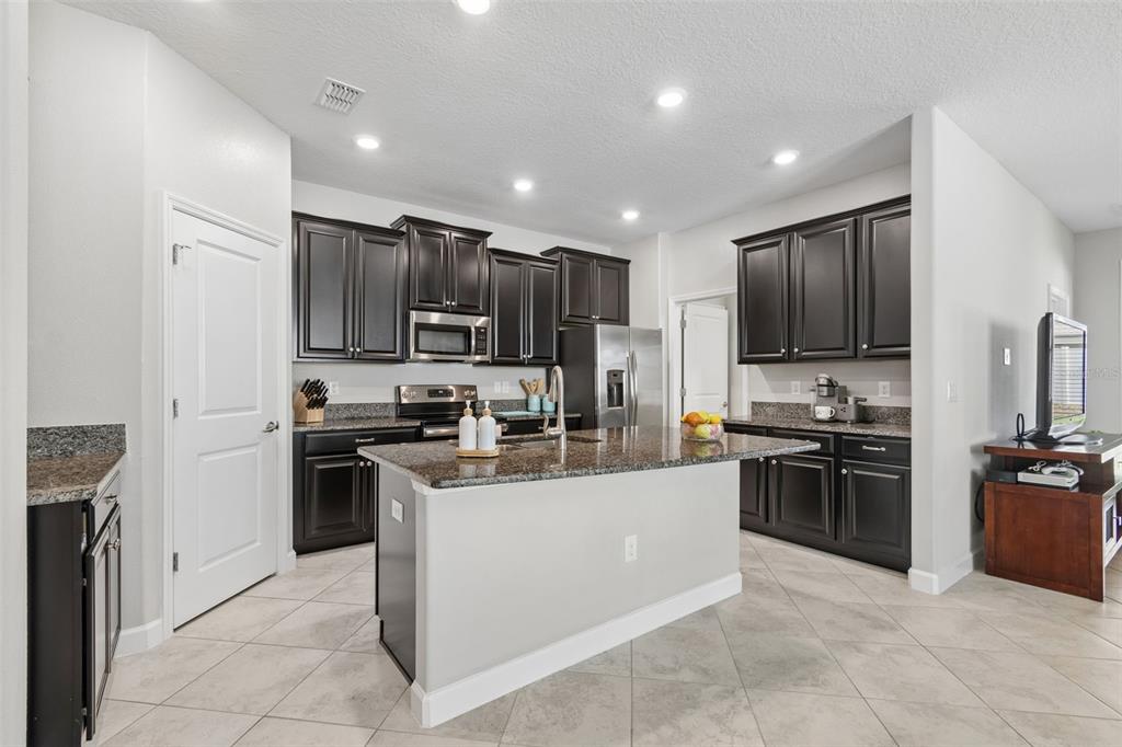 A kitchen features dark wood cabinets, granite countertops, a central island, and light tile flooring — 9908 SAGE CREEK DRIVE, RUSKIN, FL