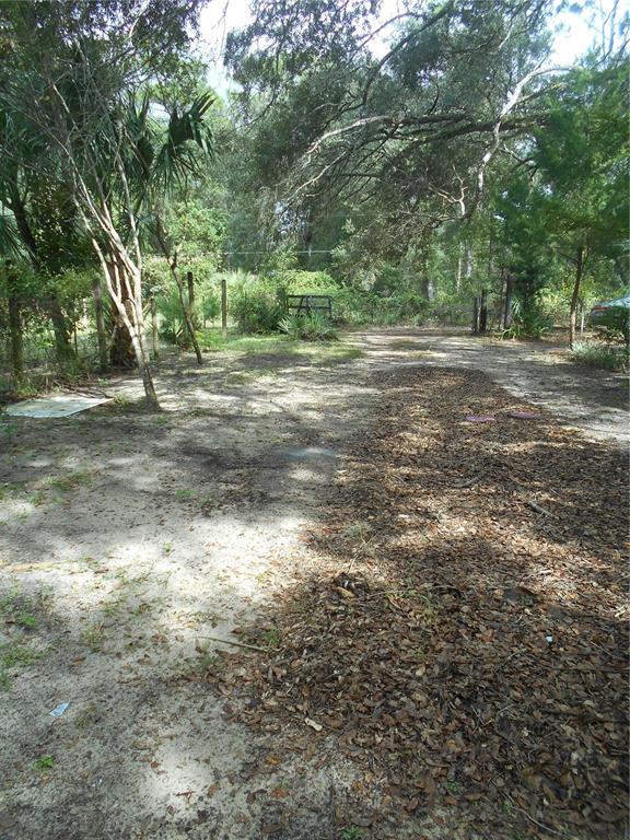 A sandy yard leads to a mobile home with a wooden ramp and blue shutters — 20425 NE 143RD STREET, SALT SPRINGS, FL
