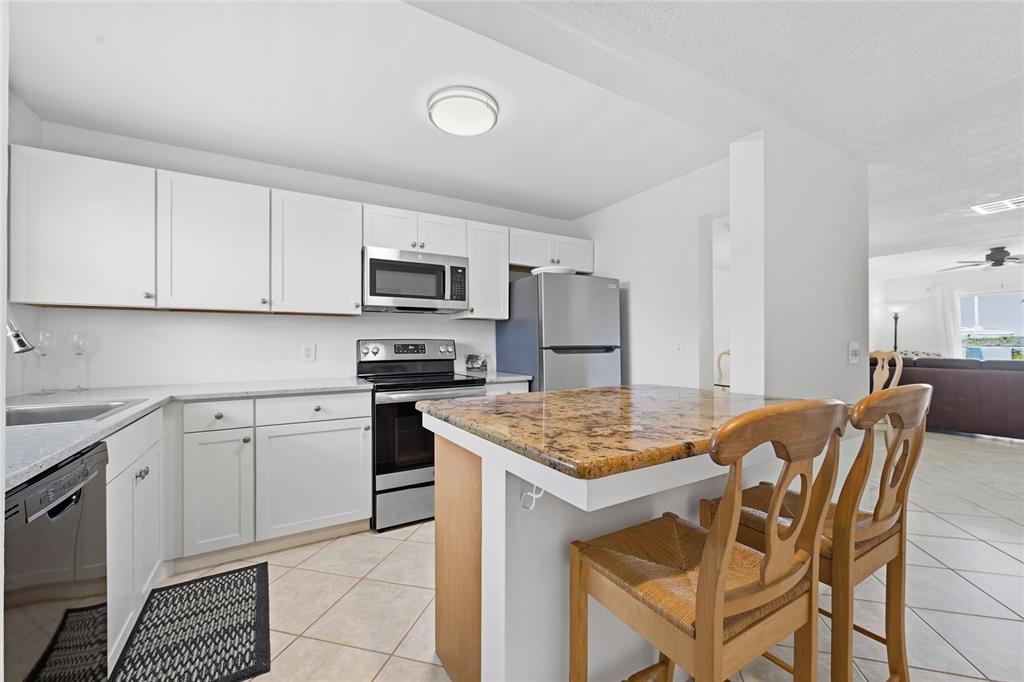 A kitchen features white cabinets, granite countertops, stainless steel appliances, and a wooden breakfast bar — 1300 SEAWAY DRIVE UNIT C1, HUTCHINSON ISLAND, FL
