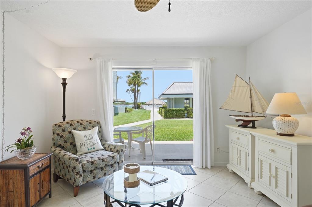 A living room features tile floors, a patterned armchair, and sliding doors opening to a patio — 1300 SEAWAY DRIVE UNIT C1, HUTCHINSON ISLAND, FL