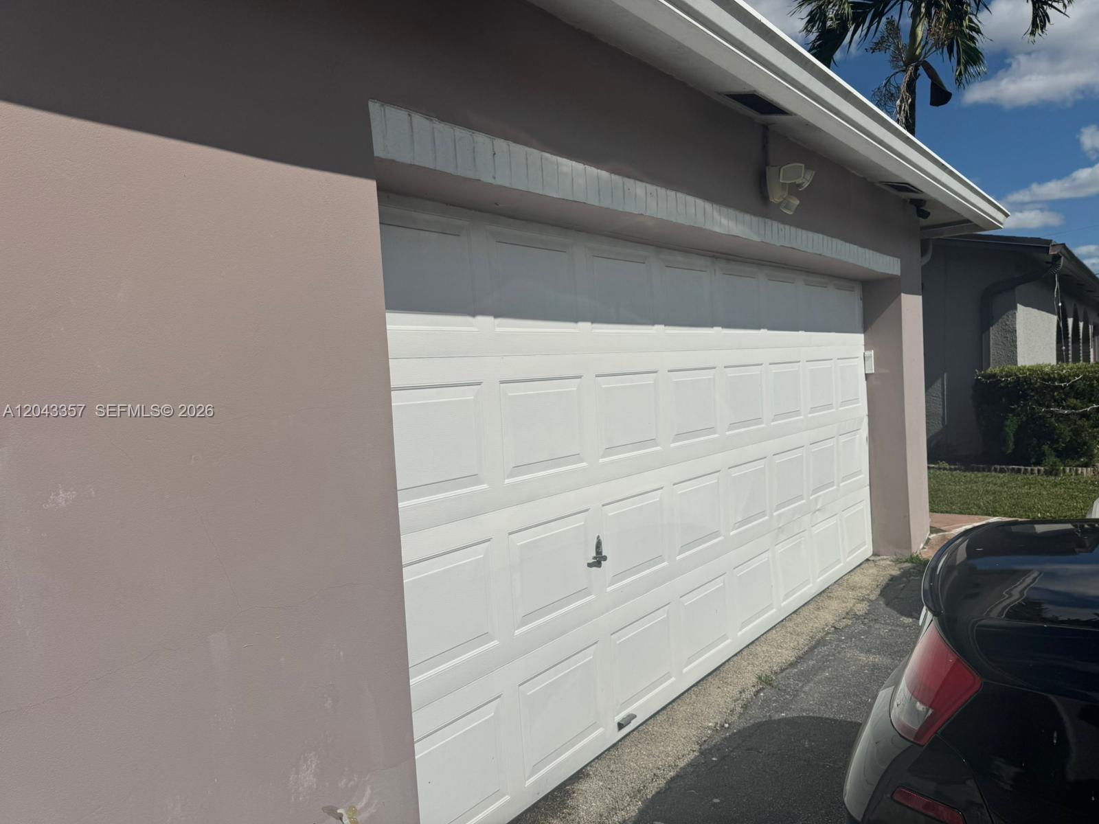 A white sectional garage door is set into the side of a pink stucco building — 9451 NW 20th Pl, Sunrise FL 33322, SUNRISE, FL