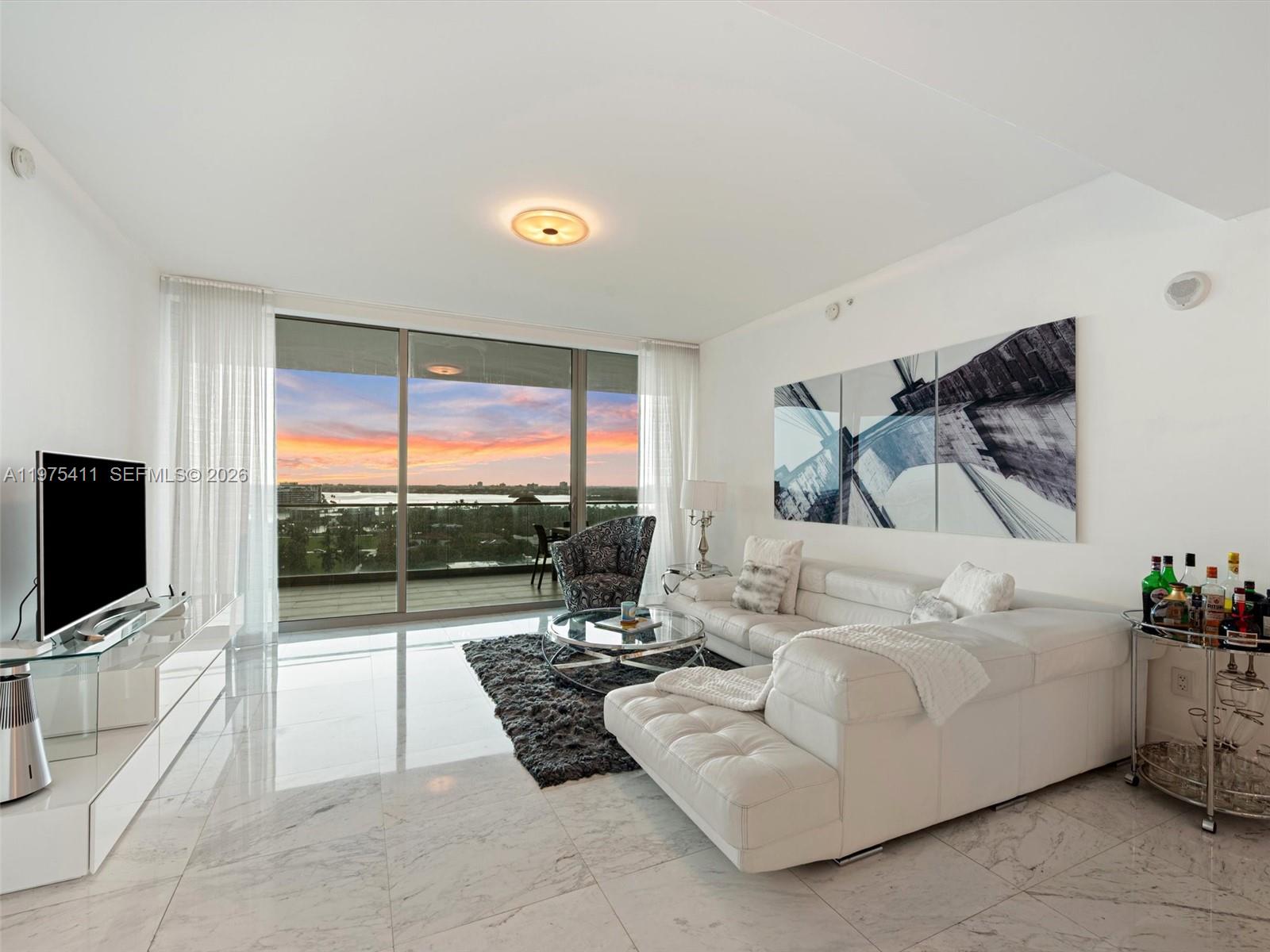A modern living room features white marble floors, a white sectional sofa, and floor-to-ceiling windows — 10203 Collins Ave # 1105, Bal Harbour FL 33154, BAL HARBOUR, FL