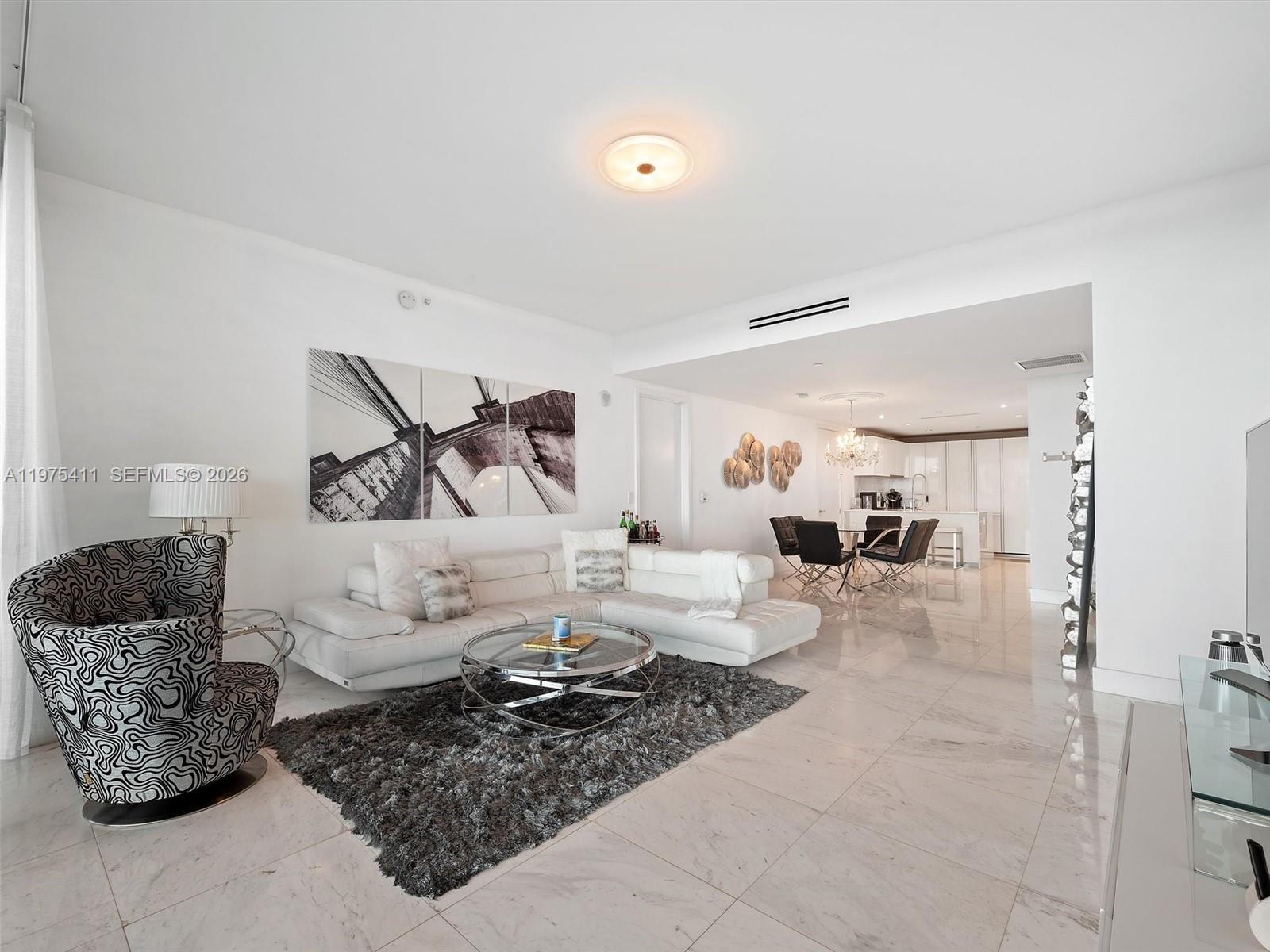 A modern living room features a white sectional sofa, patterned armchair, and marble tile flooring — 10203 Collins Ave # 1105, Bal Harbour FL 33154, BAL HARBOUR, FL