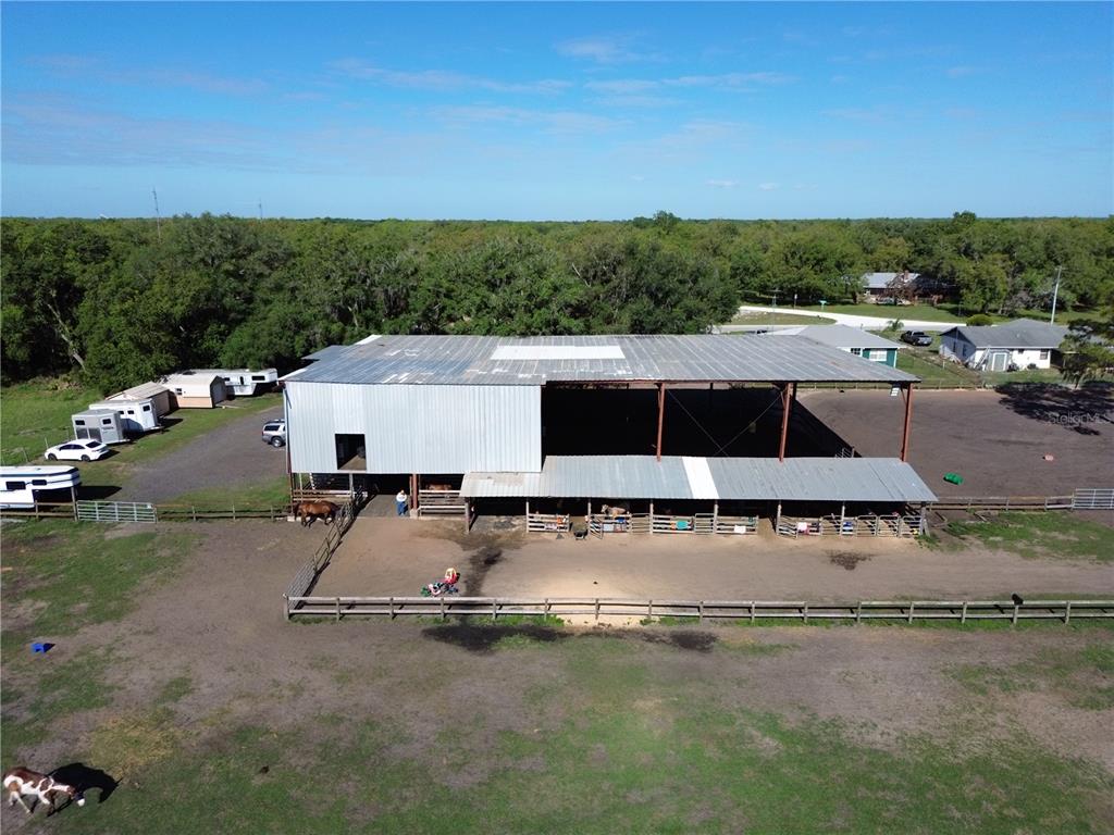 An aerial view of a large metal barn with horse stalls and an outdoor arena — 3046 N BOWDEN ROAD, AVON PARK, FL