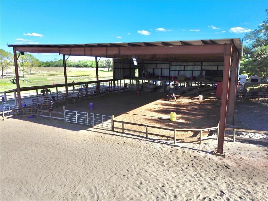 An outdoor covered horse riding arena features a dirt floor, metal fencing, and structural beams — 3046 N BOWDEN ROAD, AVON PARK, FL