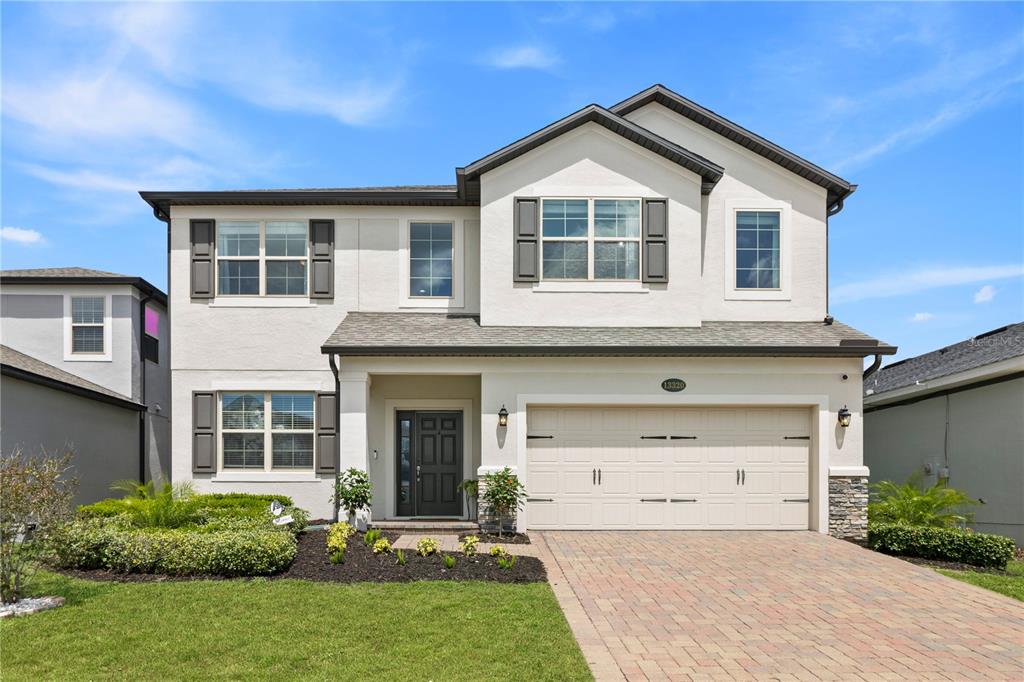 A two-story suburban house with a beige stucco exterior, a two-car garage, and landscaping — 13320 MAGNOLIA VALLEY DRIVE, CLERMONT, FL