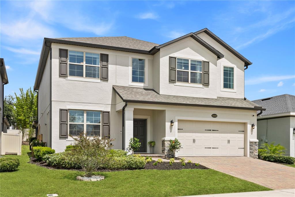 A two-story suburban house with a beige stucco exterior, a two-car garage, and landscaping — 13320 MAGNOLIA VALLEY DRIVE, CLERMONT, FL