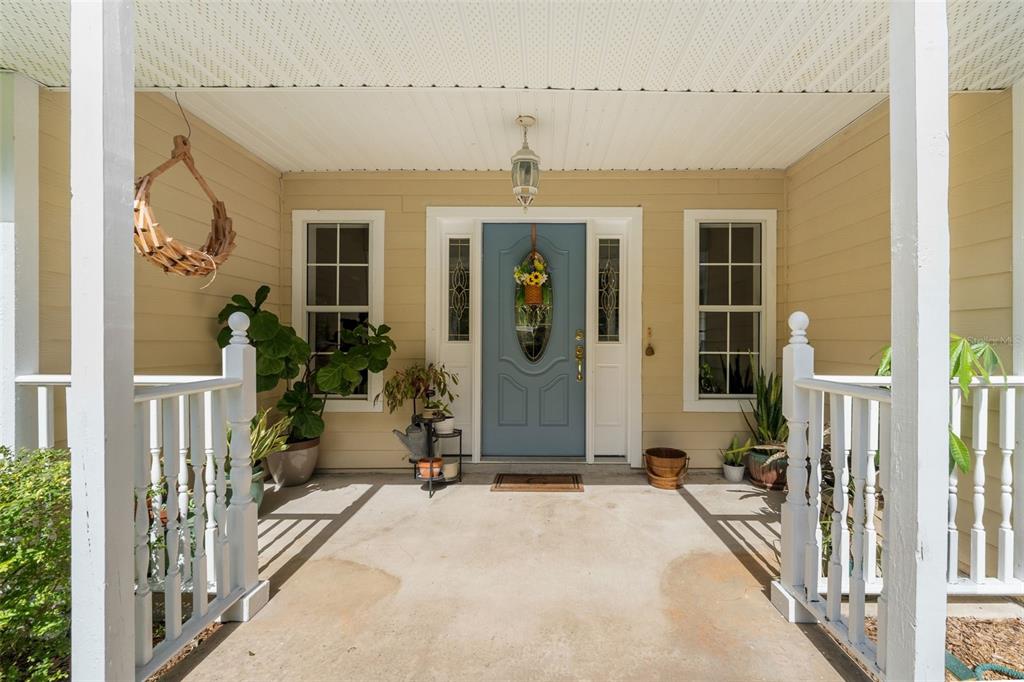 A covered front porch features a blue door, white railings, and potted plants — 646 NE 2ND STREET, WILLISTON, FL