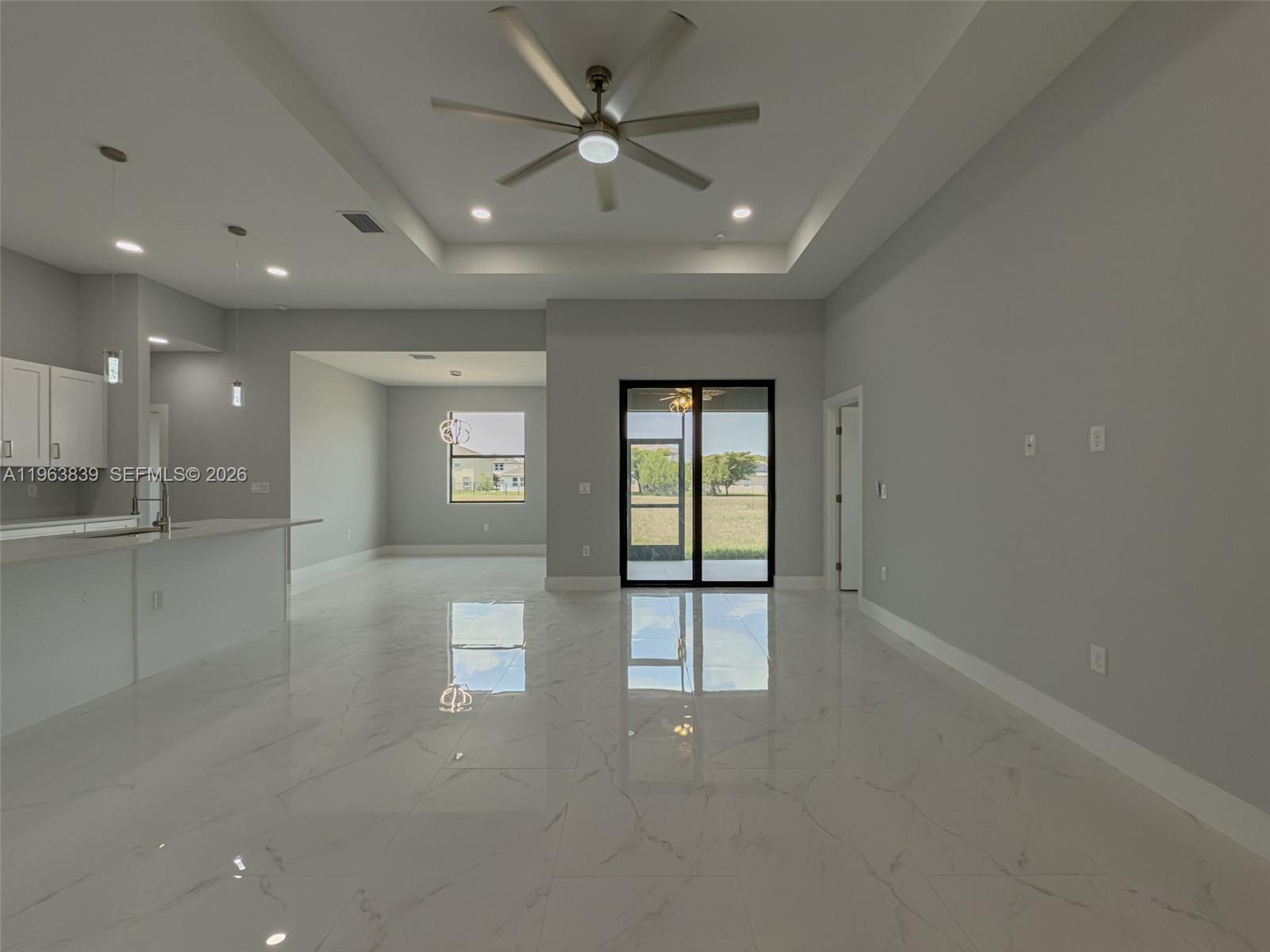 An open-concept living area features white marble-look tile flooring, a tray ceiling, and sliding doors — 417 Paddock St, Lehigh Acres FL 33974, LEHIGH ACRES, FL