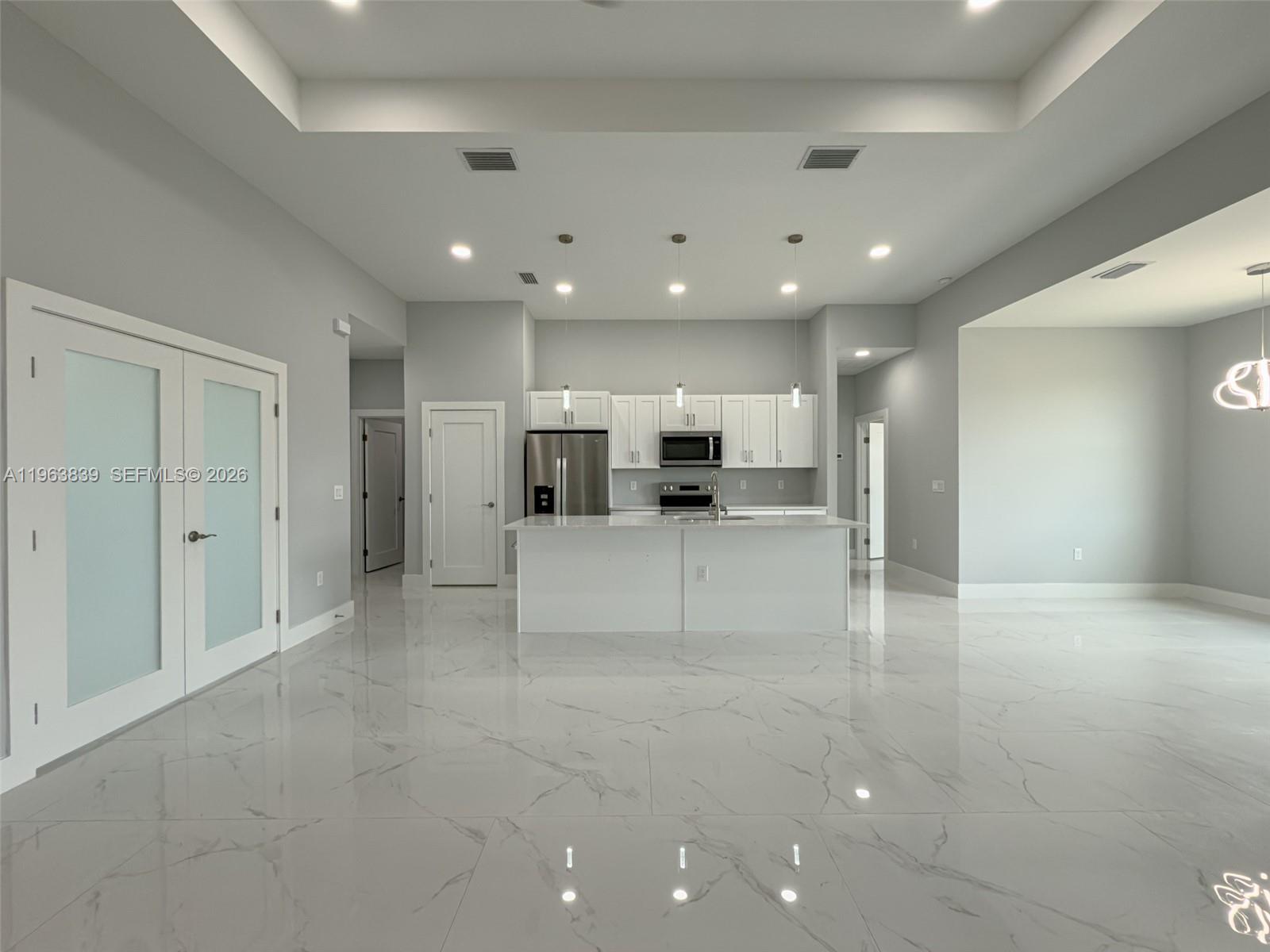 A modern kitchen features white cabinetry, a central island, and polished marble-look tile flooring — 417 Paddock St, Lehigh Acres FL 33974, LEHIGH ACRES, FL