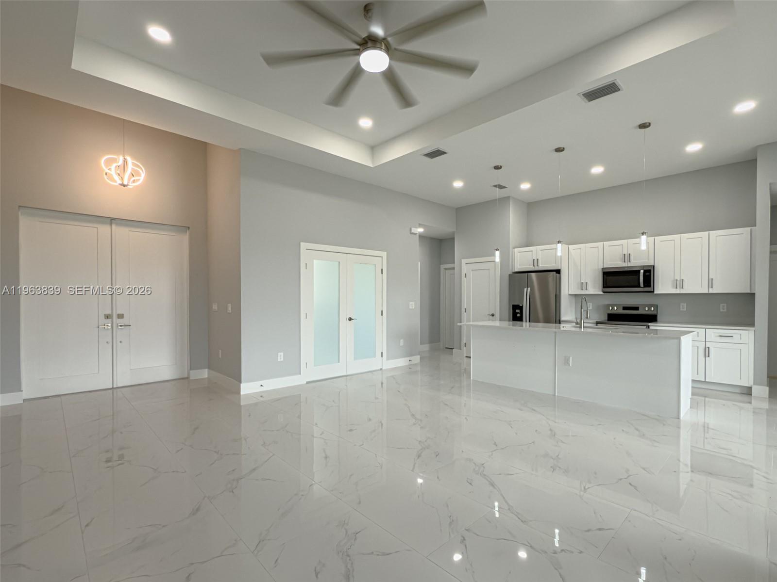 A modern kitchen with white cabinetry and marble-style tile flooring opens into a spacious room — 417 Paddock St, Lehigh Acres FL 33974, LEHIGH ACRES, FL