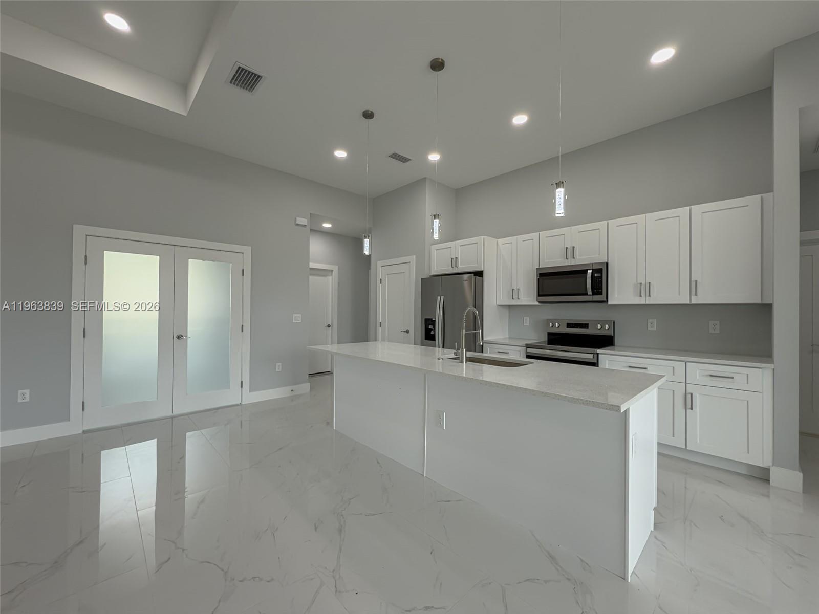 A modern kitchen features white cabinetry, a central island, and light-colored marble-style flooring — 417 Paddock St, Lehigh Acres FL 33974, LEHIGH ACRES, FL