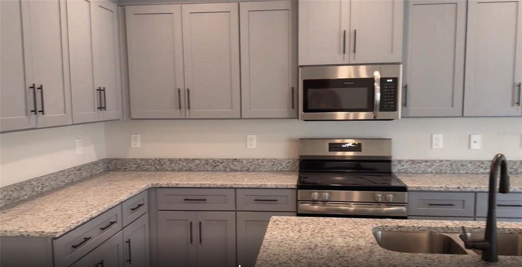 A kitchen features gray cabinets, granite countertops, stainless steel appliances, and a kitchen island — 21426 DEKALS AVENUE, PORT CHARLOTTE, FL