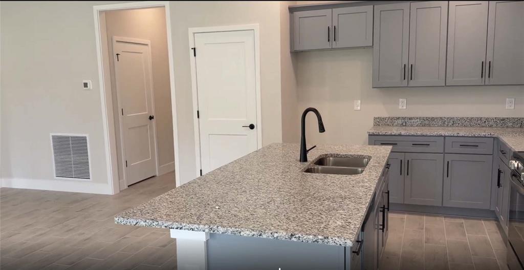 A kitchen features a granite-topped island with a sink, gray cabinets, and light wood-look flooring — 21426 DEKALS AVENUE, PORT CHARLOTTE, FL