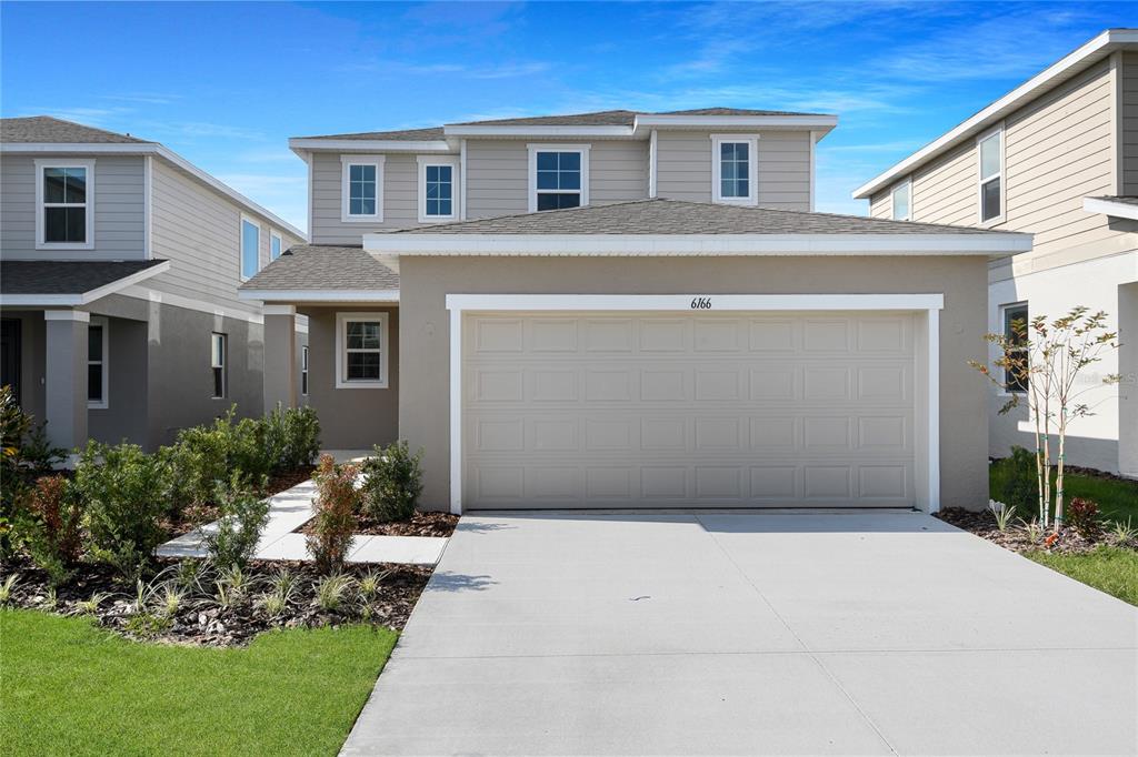 A two-story suburban house features a beige stucco facade, a two-car garage, and gray siding — 6166 DAPHNE STREET, LAKE HAMILTON, FL