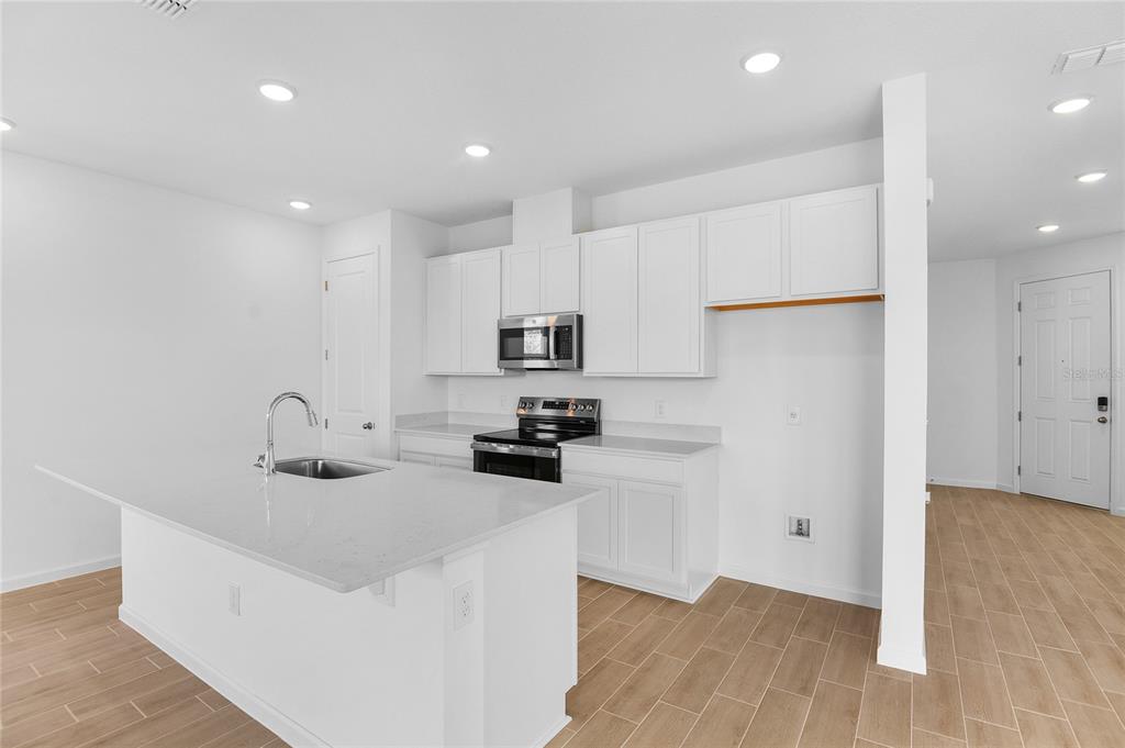 A modern kitchen features white cabinets, a quartz island, and light wood-look flooring — 6166 DAPHNE STREET, LAKE HAMILTON, FL