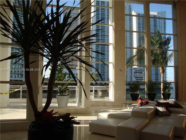 A bright lobby features a large potted plant, white modular seating, and floor-to-ceiling windows — 901 Brickell Key Blvd # 1701, Miami FL 33131, MIAMI, FL