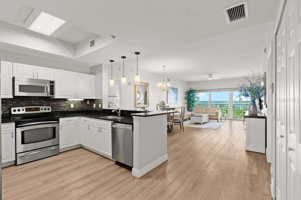 A modern kitchen with white cabinets and granite countertops opens into a bright living area — 2 OCEANS WEST BOULEVARD UNIT 702, DAYTONA BEACH, FL