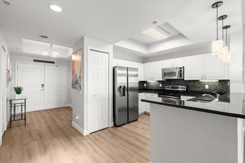 A kitchen with white cabinets, stainless steel appliances, and black countertops features light wood flooring — 2 OCEANS WEST BOULEVARD UNIT 702, DAYTONA BEACH, FL