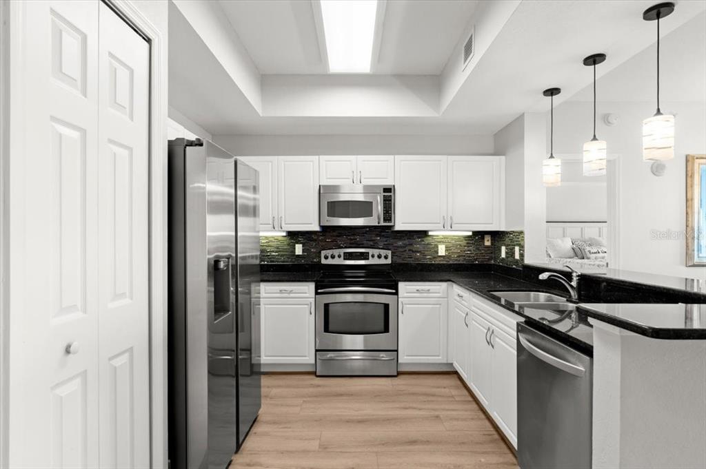 A kitchen features white cabinets, stainless steel appliances, dark countertops, and light wood-look flooring — 2 OCEANS WEST BOULEVARD UNIT 702, DAYTONA BEACH, FL