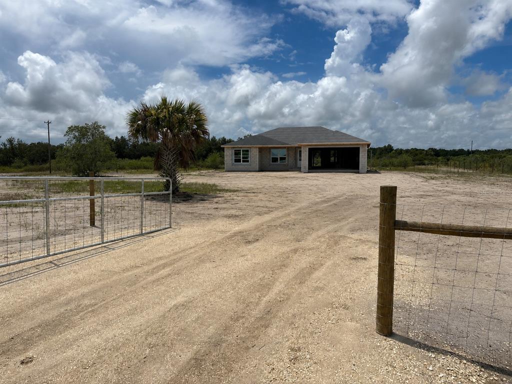 A single-story house under construction sits on a large, sandy lot behind a wire fence — 19258 NW 274TH STREET, OKEECHOBEE, FL