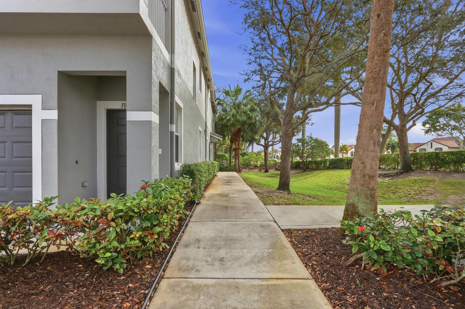 A concrete sidewalk leads along the side of a gray multi-story building with landscaping — 3108 Grandiflora Drive, FL 33467, FL