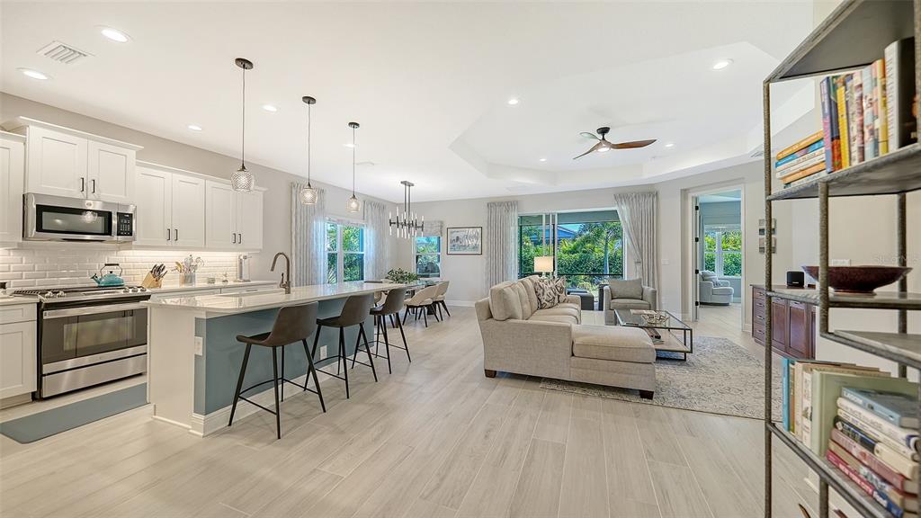An open-concept kitchen and living area with white cabinets, a large island, and tile flooring — 2550 WILD CHERRY PATH, SARASOTA, FL