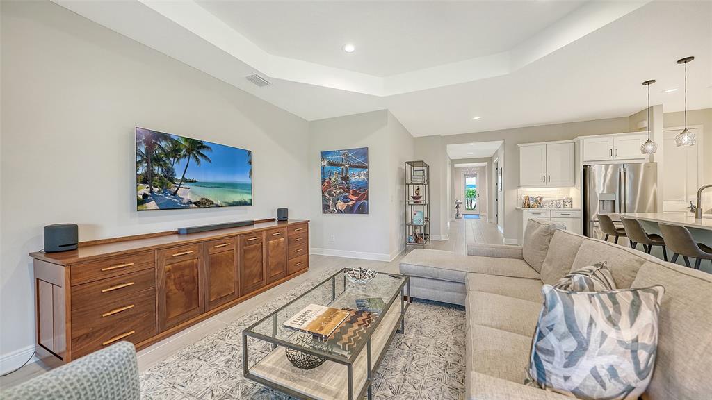 A living room features a wooden media console, a sectional sofa, and an open kitchen — 2550 WILD CHERRY PATH, SARASOTA, FL