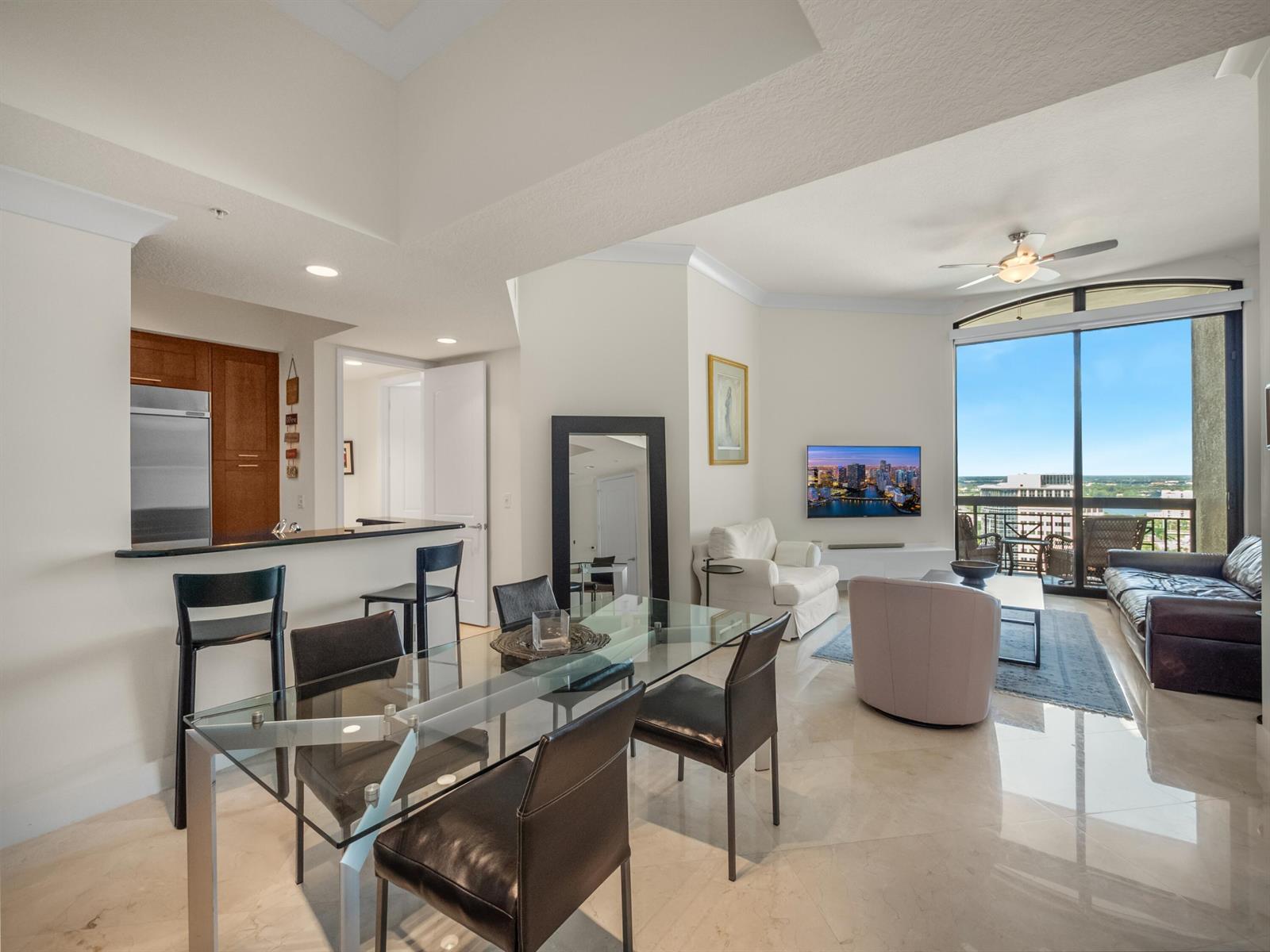 An open-concept living and dining area features a glass table, bar seating, and floor-to-ceiling windows — 701 S Olive Avenue # 2117, West Palm Beach FL 33401, WEST PALM BEACH, FL
