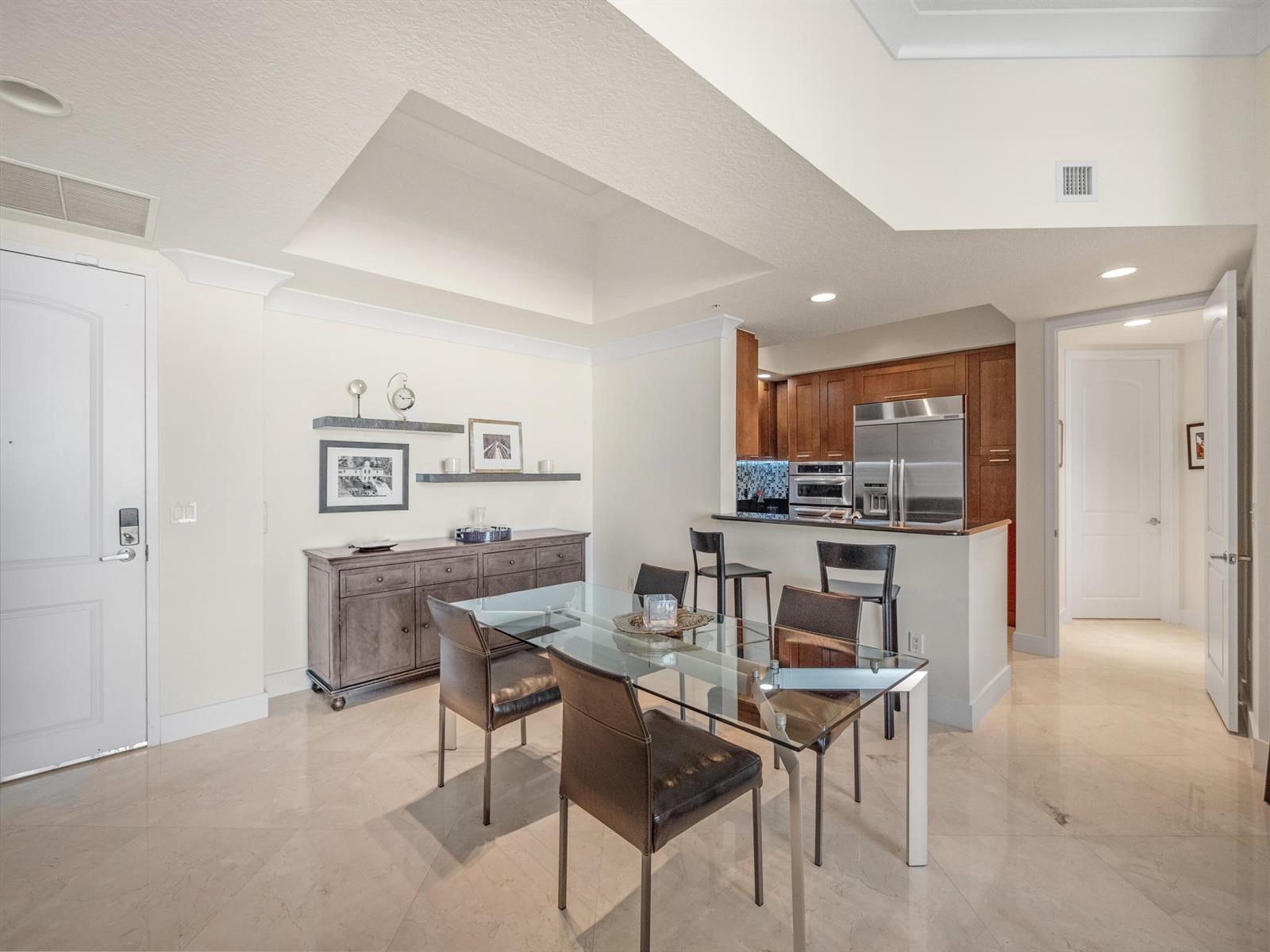 A dining area with a glass table and sideboard sits adjacent to a kitchen island — 701 S Olive Avenue # 2117, West Palm Beach FL 33401, WEST PALM BEACH, FL