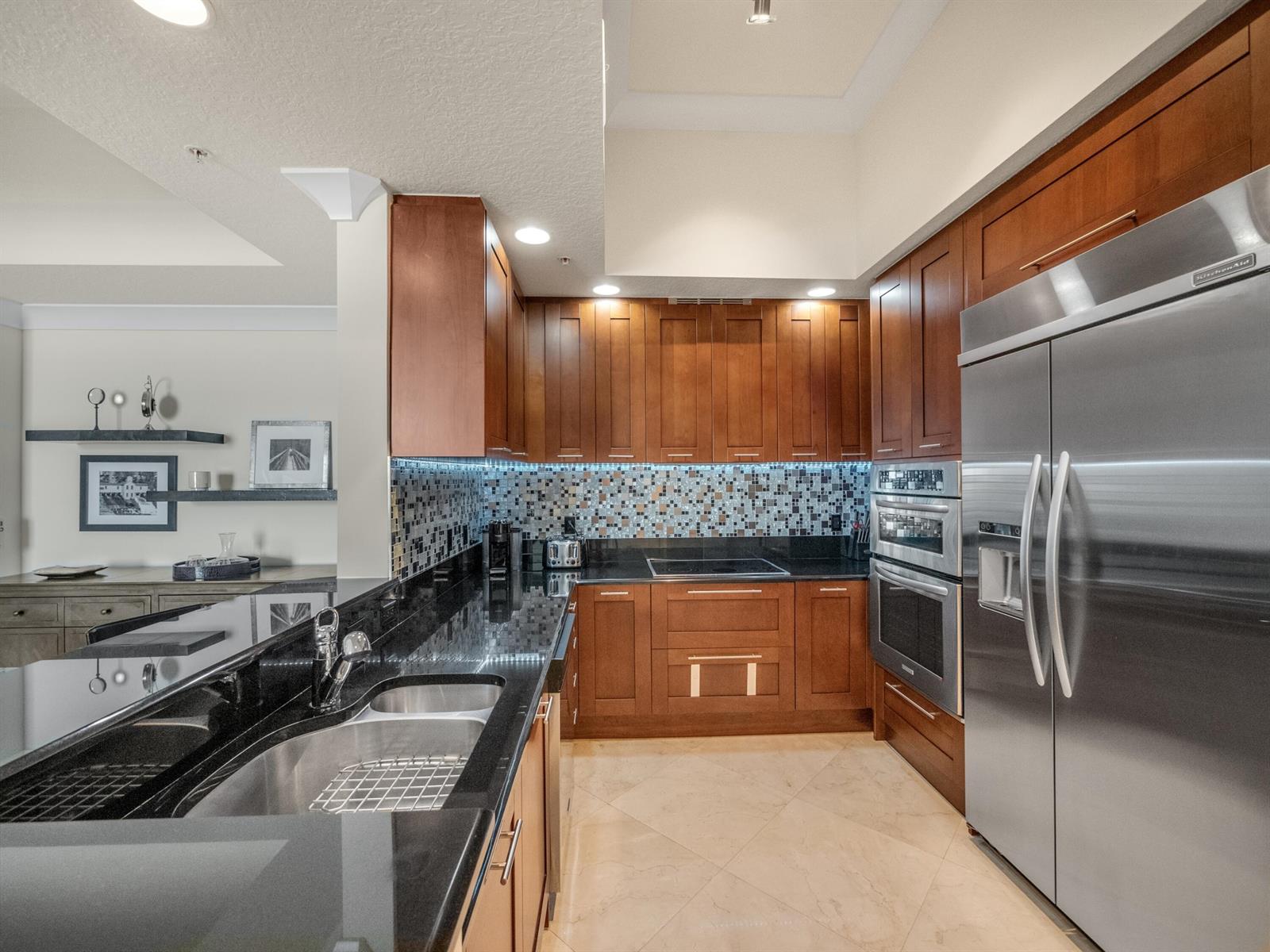 A kitchen features dark wood cabinets, black granite countertops, stainless steel appliances, and a mosaic backsplash — 701 S Olive Avenue # 2117, West Palm Beach FL 33401, WEST PALM BEACH, FL