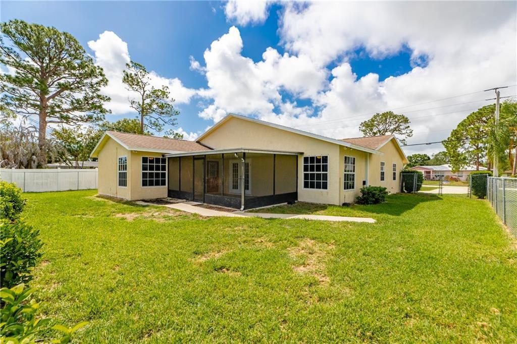 The exterior of a tan house features a screened-in porch and a large grassy backyard — SEBASTIAN, FL