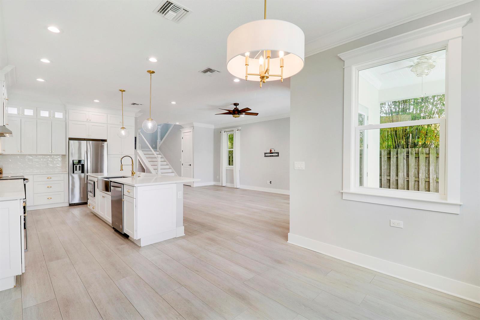 A bright, open-concept kitchen and living area with white cabinetry, light wood floors, and pendants — 3997 SE Barcelona Street, Stuart FL 34997, STUART, FL