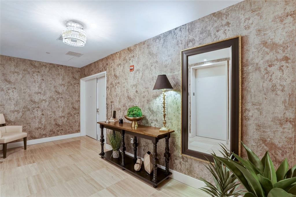 A hallway features textured brown wallpaper, a wooden console table, a large mirror, and lighting — 3101 BAYSHORE BOULEVARD UNIT 504, TAMPA, FL