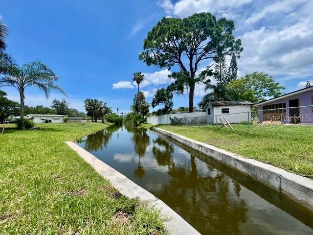 A narrow canal flows between grassy banks with palm trees and houses in the background — 5113 AVERY ROAD, NEW PORT RICHEY, FL