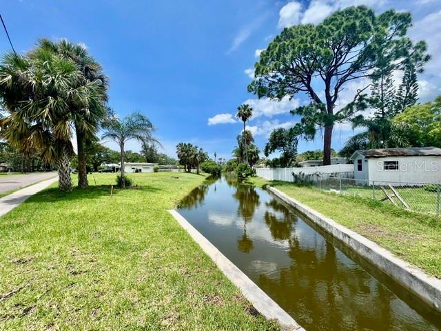 A narrow canal flows between a grassy yard and a small white house — 5113 AVERY ROAD, NEW PORT RICHEY, FL