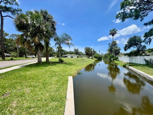 A grassy lawn borders a narrow canal with palm trees under a blue sky — 5113 AVERY ROAD, NEW PORT RICHEY, FL
