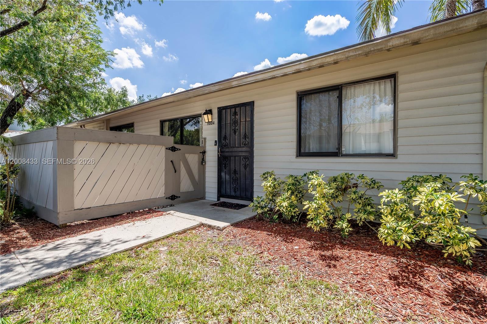 The exterior of a single-story home features light-colored siding, a metal security door, and a fence — 9804 NW 37th St # 3E, Sunrise FL 33351, SUNRISE, FL